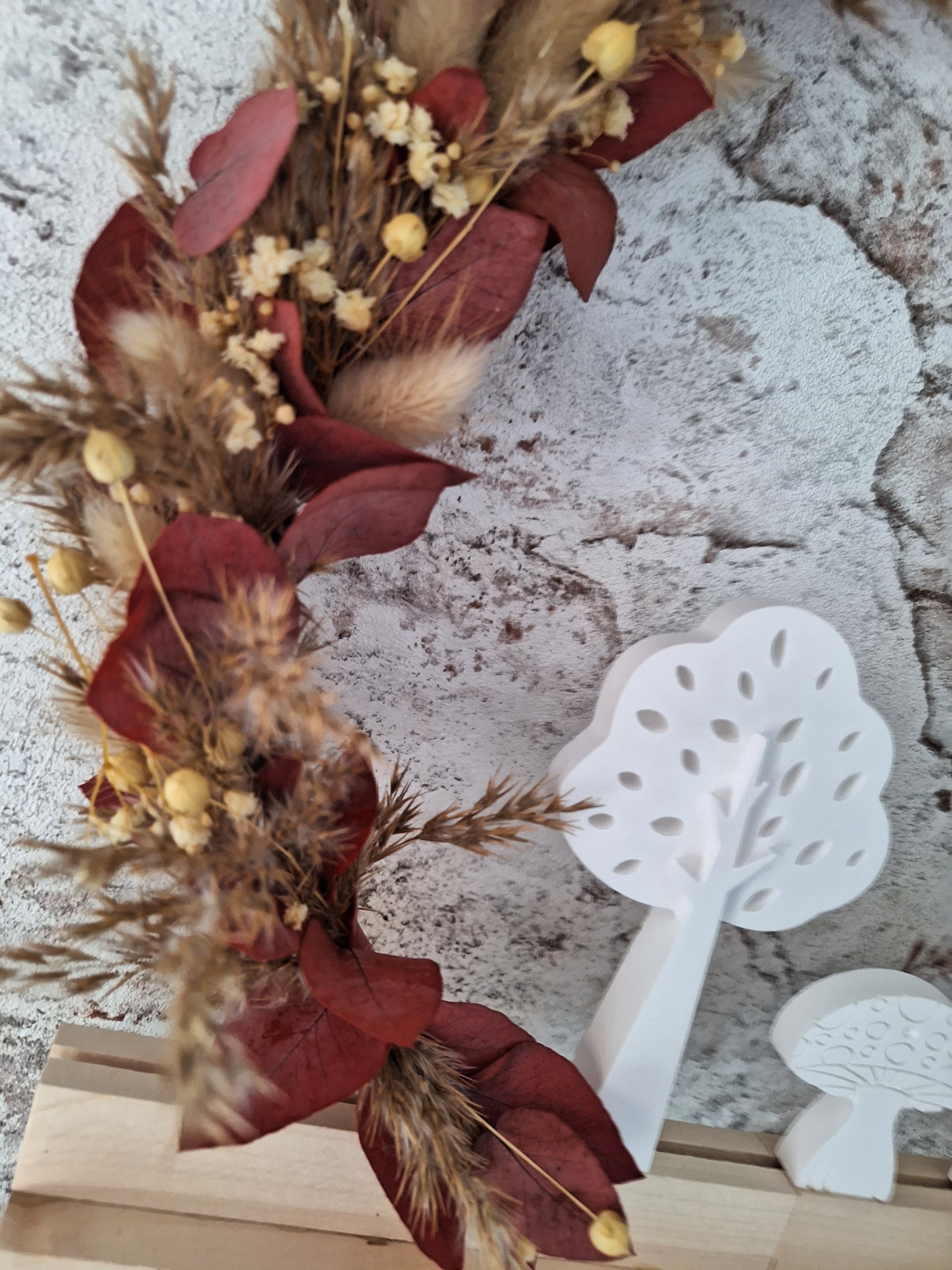 Herbstlicher Dekoaufsteller mit Trockenblumen in Rot- und Brauntönen, weißen Keraflottfiguren in Form von zwei Bäumen und einem Pilz, auf einem Holzsockel helles Holz und Weißer Metallring, handgefertigt und ideal für die saisonale Dekoration.
das bild zeigt eine Nahaufnahme der Trockenblumen.