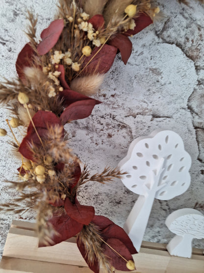 Herbstlicher Dekoaufsteller mit Trockenblumen in Rot- und Brauntönen, weißen Keraflottfiguren in Form von zwei Bäumen und einem Pilz, auf einem Holzsockel helles Holz und Weißer Metallring, handgefertigt und ideal für die saisonale Dekoration.
das bild zeigt eine Nahaufnahme der Trockenblumen.