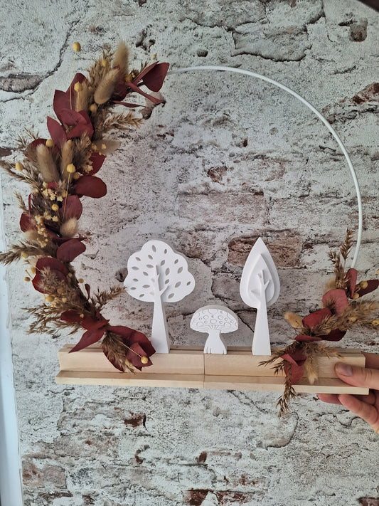 Herbstlicher Dekoaufsteller mit Trockenblumen in Rot- und Brauntönen, weißen Keraflottfiguren in Form von zwei Bäumen und einem Pilz, auf einem Holzsockel helles Holz und Weißer Metallring, handgefertigt und ideal für die saisonale Dekoration.
Die Trockenblumen sind links vom Holzsockel bis oben und rechts vom Holzsockel circa zehn zentimeter hoch.