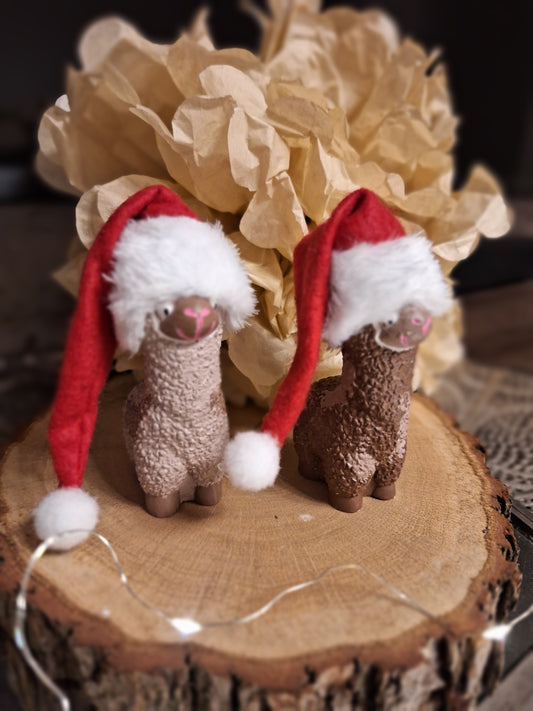 Gezeigt wird ein aus Keralott gegossenes und handbemaltes Alpaka den  Farben braun beige gezeigt. Auf dem Kopf des Alpaka ist eine Rote Weihnachtsmütze mit Weißer Bommel und Weißen Bund. Die Mütze ist lang und fällt seitlich am Alpaka herunter.