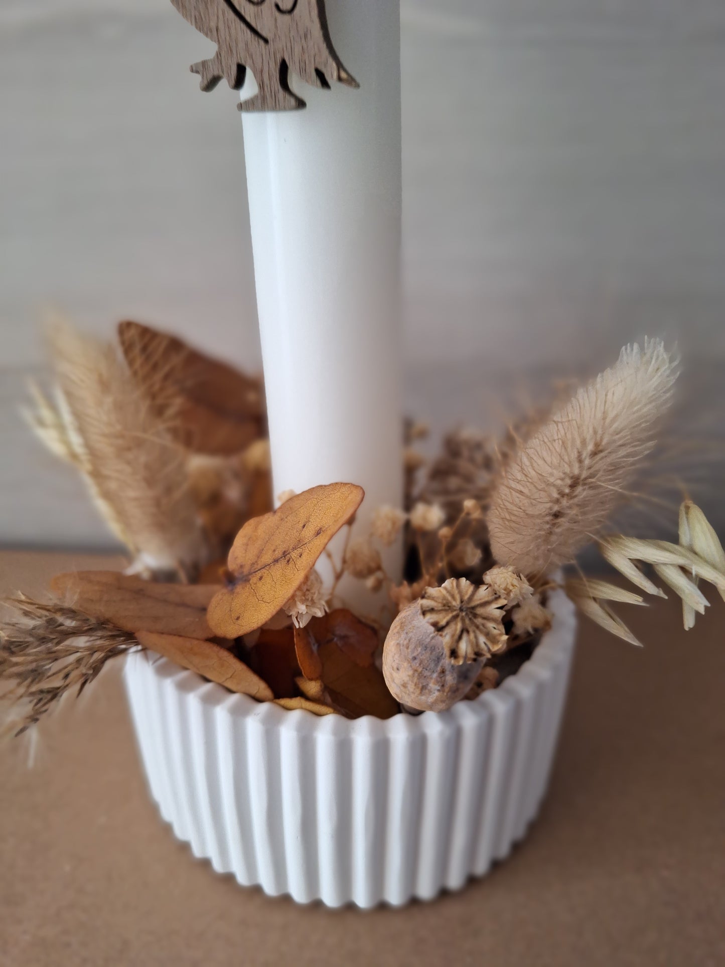 Herbstliches Gesteck in einer kleinen weißen Rillen-Schale mit Trockenblumen, einer Stabkerze mit Eulen-Anhänger als Dekoration