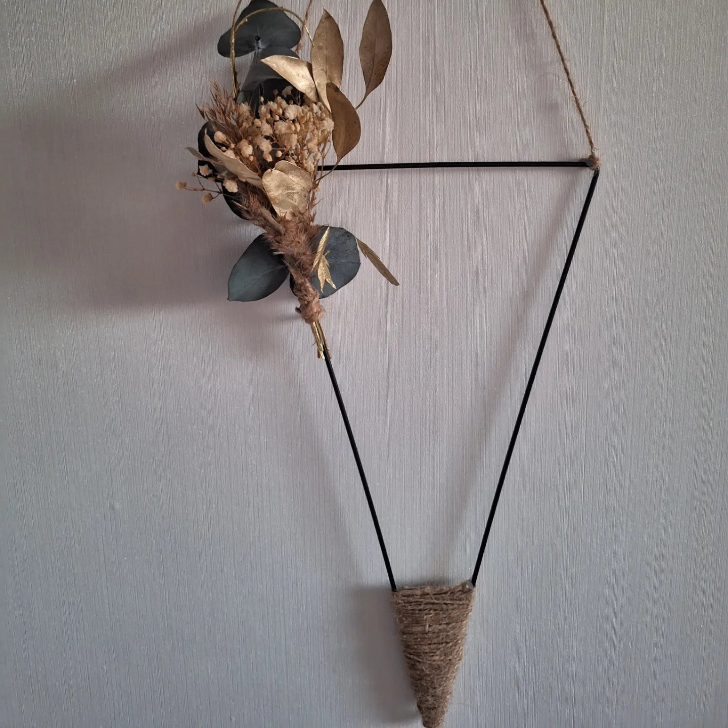 Moderne Wanddekoration aus dreieckigem Metallrahmen mit Trockenblumen und Jute – stilvolle Innendekoration