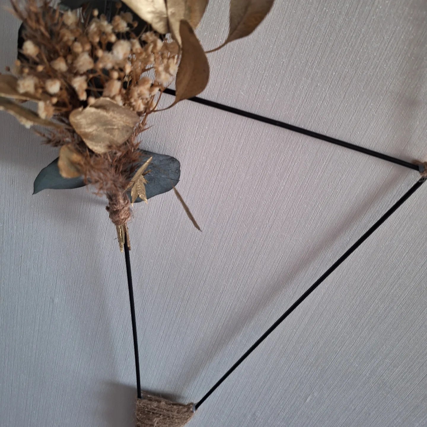 Moderne Wanddekoration aus dreieckigem Metallrahmen mit Trockenblumen und Jute – stilvolle Innendekoration