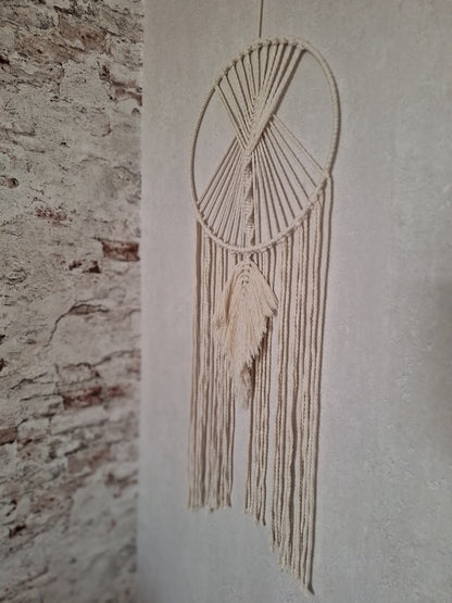 Handgefertigte cremefarbene Makramee-Wanddekoration an einem eleganten Metallring, ideal für Boho- und moderne Wohnräume, bringt Wärme und Stil in dein Zuhause. Die Farbe des Makramee Garns ist beige. der Metallring ist mit Garn umwickelt. Unter dem Ring hängen Makramee Garn Schnüre hinab und mittig eine Makramee Feder in locker fallend