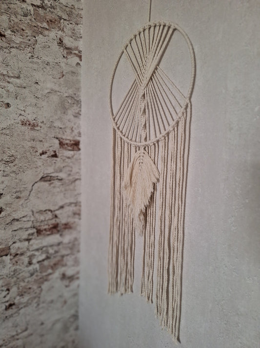 Handgefertigte cremefarbene Makramee-Wanddekoration an einem eleganten Metallring, ideal für Boho- und moderne Wohnräume, bringt Wärme und Stil in dein Zuhause. Die Farbe des Makramee Garns ist beige. der Metallring ist mit Garn umwickelt. Unter dem Ring hängen Makramee Garn Schnüre hinab und mittig eine Makramee Feder in locker fallend