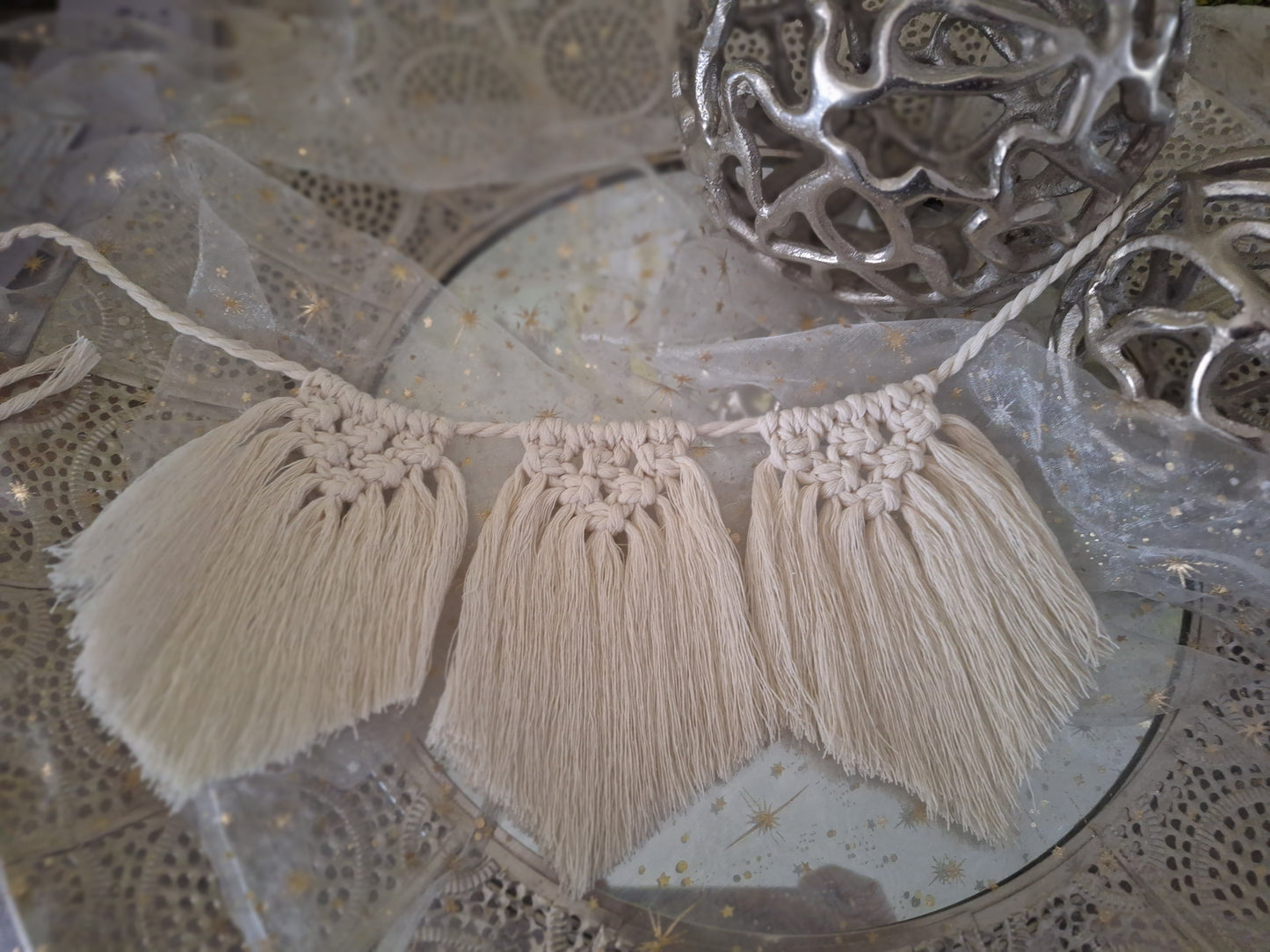 Gezeigt ist eine Makramee Wimpelkette im Boho-Stil in beige. Es sind drei Flechtteile bei diesem Beispiel. oben ist zu einem Dreieck geknüpft und der Rest fällt glatt zu einer leichten Spitze herab.