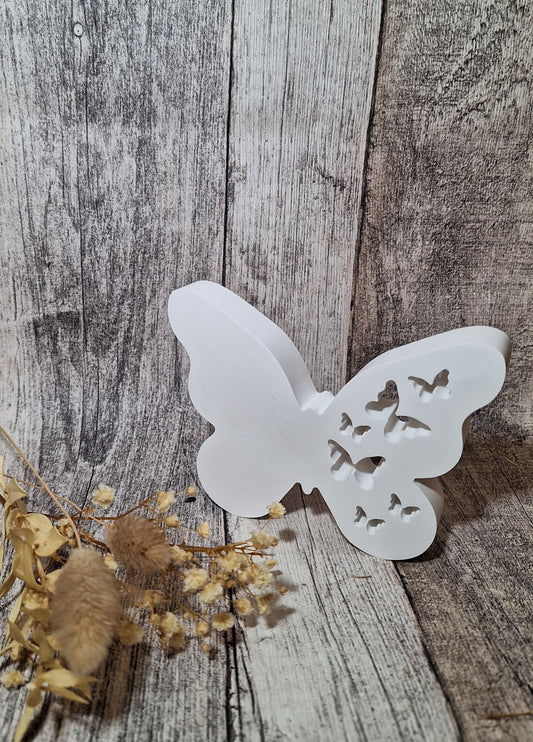 Gezeigt ist ein weißer aus Keraflott gefertigter Schmetterling. Eine Flügelseite ist glatt und eine ist mit Löchern in Form von Schmetterlingen versehen.  