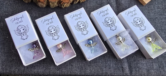 Kleiner Schutzengelanhänger gefertigt aus Perlen. Liegt in einer kleinen Schachtel gebettet auf Watte. Auf der Schachtel ist ein Aufkleber mit dem Spruch "Schutzengel für dich" und einem Bild eines kleinen Engelmädchens. Farben:lila, rosa, blau, gelb,weiß