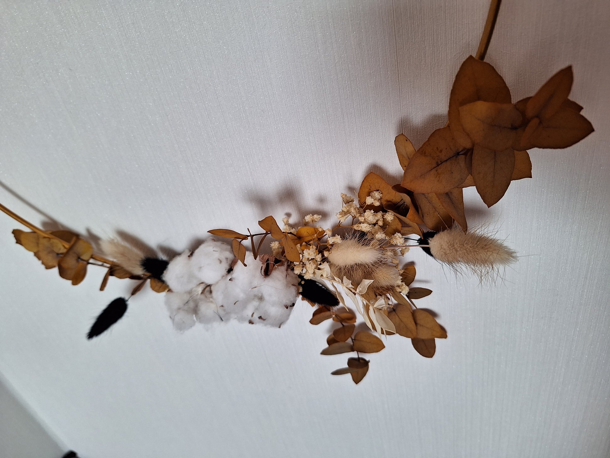 Stilvolle Wand- oder Fenstergestaltung mit einem goldenen Metallring, dekoriert mit Trockenblumen und Trockendeko in Braun- und Beigetönen.
