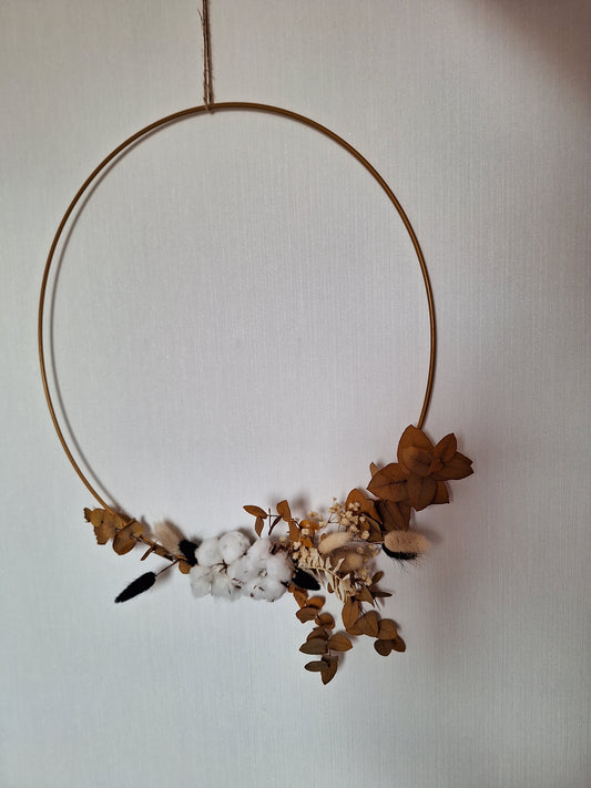 Stilvolle Wand- oder Fenstergestaltung mit einem goldenen Metallring, dekoriert mit Trockenblumen und Trockendeko in Braun- und Beigetönen.