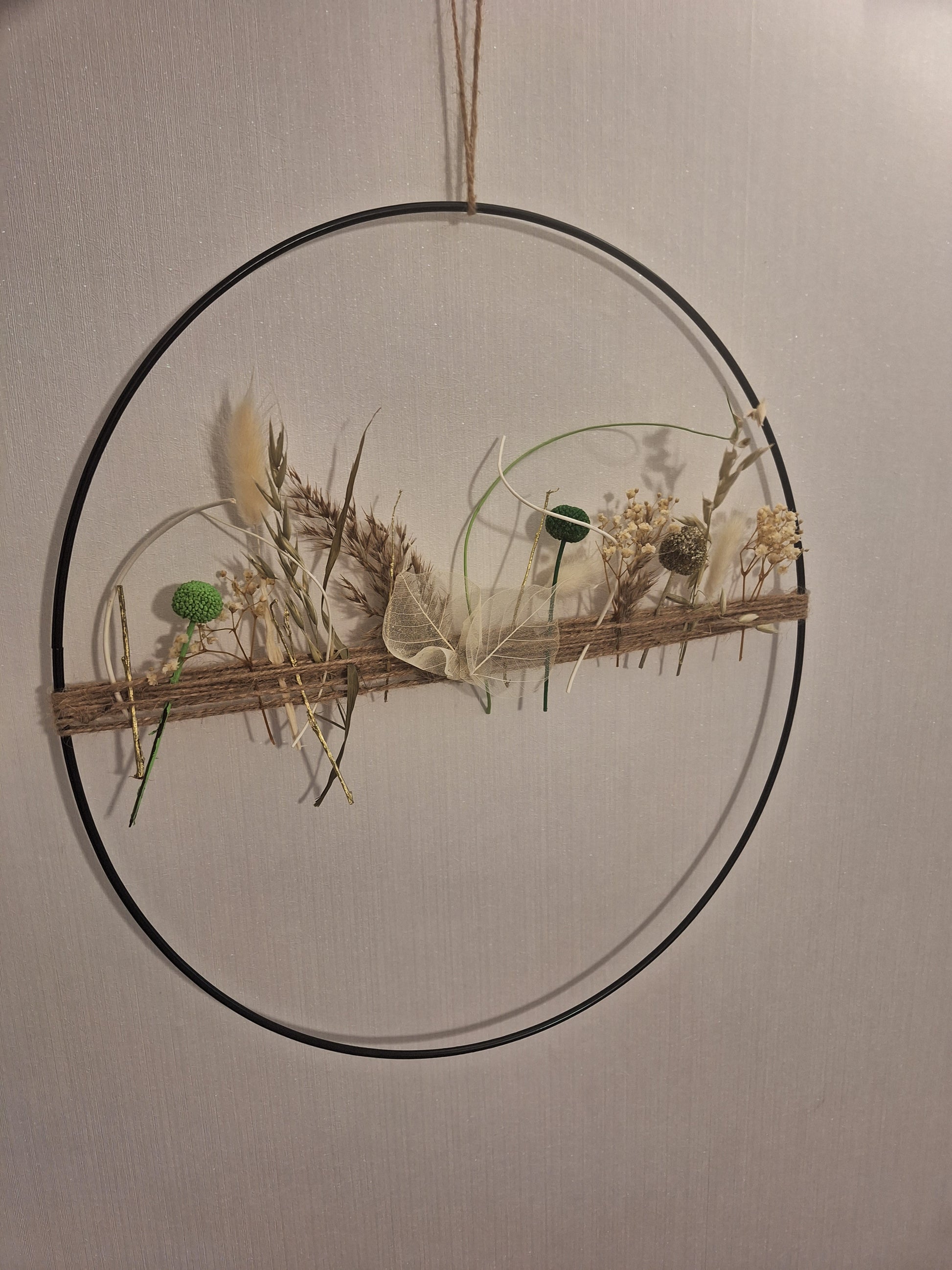 Dekorative Metallring-Arrangierung mit bunten Trockenblumen, befestigt an einem Juteband, ideal als moderne Wand- oder Fenstergestaltung für frische Akzente im Zuhause.