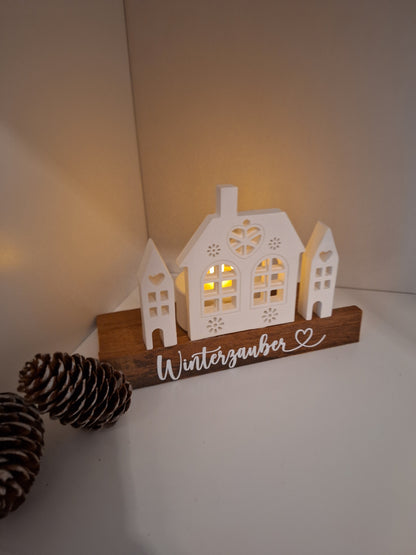 Dekoaufsteller mit Häusern welche indirekt beleuchtet werden können durch Teelichthalter dahinter. Steht auf Holzsockel. 